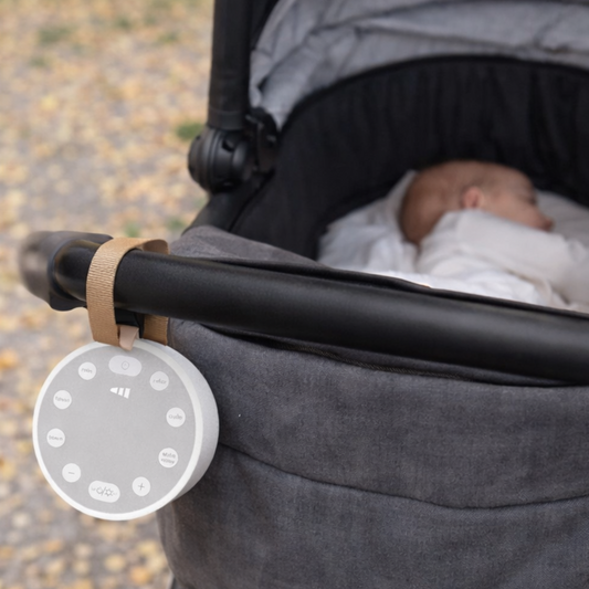 Stroller with a baby and a white noise device attached to the handle.